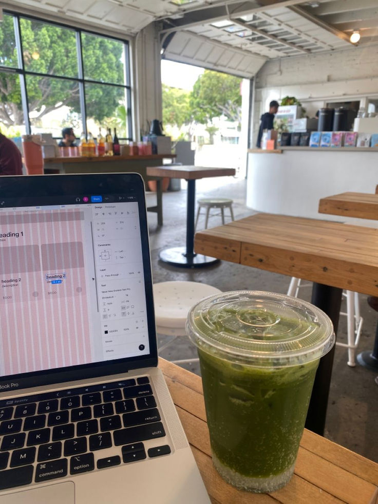 Laptop with a Figma design open beside a drink in a cafe workspace